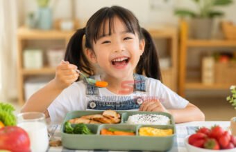 Seorang anak menikmati menu makan siang sehat berisi nasi, ayam, sayuran, telur, dan buah di meja makan dengan suasana ceria. (Foto: dok previews.sriwijayaterkini.id)